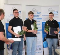 Auszubildende stehend vor den RollUps des Ausbildungszentrum Zwickau mit Abschlusszeugnis und Blumen in den Händen. 