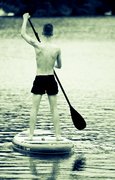 Mann steht aufrecht auf einem schwimmfähigen Board mit einem Paddel in der Hand
