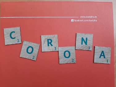 Im Bild sind sechs Buchstabentafeln auf orangem Grund zu sehen, die das Wort "Corona" bilden.
