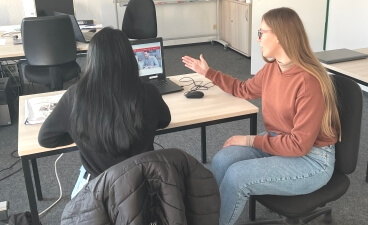Teaserbild: Daria Filonenko sitzt rechts neben einer Teilnehmerin. Beide schauen auf ein Notebook, auf dem die Jobsuche der Agentur für Arbeit geöffnet ist.