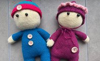 Zwei gehäkelte Puppen, links mit blauem Anzug und rot-blauer Mütze, rechts mit dunkelrotem Anzug und dunkelroter Mütze. 
