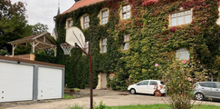 Innenhof mit begrüntem, efeubewachsenem Gebäude, Basketballkorb, Garagentoren und geparkten Autos vor der Fassade.