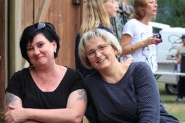 im Vordergrund sitzen zwei Frauen lachend nebeneinander, im Hintergrund zwei Frauen stehend. 