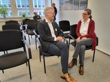 Foto: Eine Mann und eine Frau sitzen in einem Raum nebeneinander und unterhalten sich lächelnd