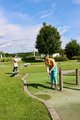 Sommerfest 2026 Zwei Mitarbeiterinnen beim Minigolf spielen. Im Hintergrund blauer Himmel mit Wolken und Bäume.