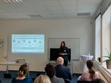 Foto: Eine Frau referiert neben einer Power Point Präsentation stehend zum Thema Teilqualifizierung.