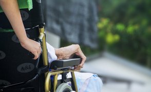 Pfleger bewegt eine alte Frau im Rollstuhl