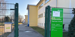 Eingang eines Gebäudekomplexes mit Metallzaun und grünem Schild „SOS-Kinderdorf Sachsen-Anhalt – Kinder-, Jugend- und Familienzentrum Güsten“