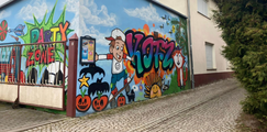 Foto: Bunte Graffitis mit Comicfiguren, Schriftzügen wie „Party Zone“, „KJFZ“ und Tiermotiven an der Außenwand eines Gebäudes.