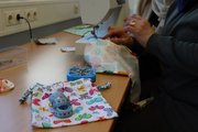 Foto: Eine Teilnehmerin arbeitet an der Nähmaschine mit buntem Stoff, Maßband und Stecknadeln.