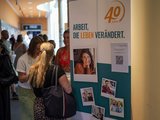 Fachtagung Depression Foto vom Roll-Up der faw samt Stehtisch, an dem mehrere Personen im Gespräch sind.