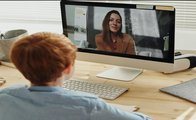 Ein Grundschüler sitzt vor dem PC und wird von seiner Lehrerin beschult.