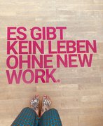 Am unteren Bildrand sind zwei nackte, tätowierte Frauenfüße. Davor steht auf dem Fußboden: "Es gibt kein Leben ohne New Work".