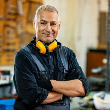 Ein Mann steht lächeln in einer Werkstatt: Symbolbild Berufliche Rehabilitation