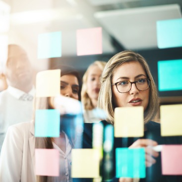 Eine Gruppe Seminar-Teilnehmer*innen steht vor einer Glaswand mit Klebezetteln: Symbolbild Weiterbildung