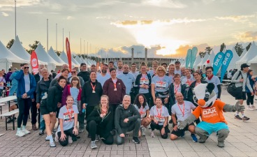 Foto: Das Team von faw und BTZ im Abendlicht und Stadion mit Maskottchen der DAK
