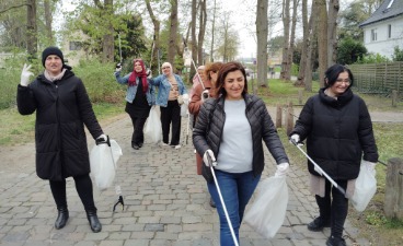 Foto: mehrere Personen ausgestatett mit Greifzangen und Müllbeuteln beim Müllsammeln in der Natur. 