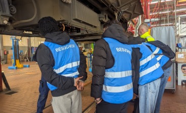 Foto: Besucher*innen schauen im Betrieb unter der S-Ban auf einer Hebebühne