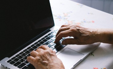 Hände einer ältere Person auf Computertastatur.