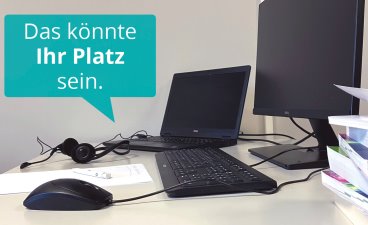 Fotografiert wurde ein Schreibtisch mit einem Laptop, einem großen Bildschirm, einer Maus und Tastatur, einem Notizblatt und einem Stapel Bücher. Darüber steht in einer Sprechblase: Das könnte Ihr Platz sein.