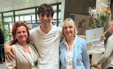 Zwischen Frau Reitzenstein (links) und Frau Falke-Nossing (rechts) steht unser Auszubildender Carlos. Er hat die Arme um die Schultern beider Frauen gelegt und hält rechts stolz sein Zeugnis und einen Blumenstrauß in der Hand.