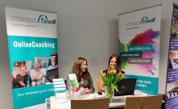 Bildungsmesse im Jobcenter Dresden Zwei Frauen am Tisch der faw Dresden, hinter ihnen zwei RollUps der faw. Davor auf dem Tisch diverse Materialien der faw.