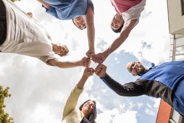 Beispielbild Teambildung: Fünf Personen stehen im Kreis und strecken die Arme zur Mitte, ihre Fäuste berühren sich.