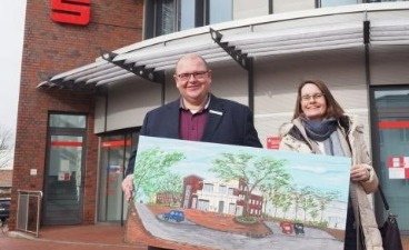 Mann und Frau stehen vor dem Gebäude der Sparkasse und halten eine Bild in die Kamera.