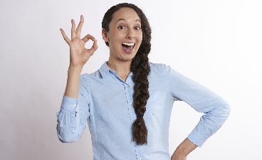 Frau mit Zopf macht das OK-Zeichen mit Daumen und Zeigefinger