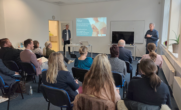 Vortrag zu ETAPP, mehere Teilnehmende schauen auf eine Bildpräsentation, zwei Männer stehen vorne, einer spricht zu den Teilnehmenden