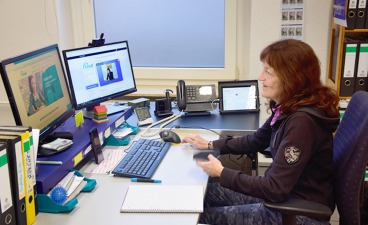 Frau sitzt am Schreibtisch mit zwei Monitoren vor sich und führt einen Technikcheck durch.