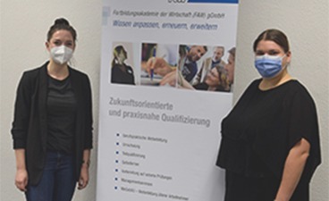 Zwei junge Frauen mit Mund-Nasen-Bedeckung stehen neben einem Flipchart der FAW.