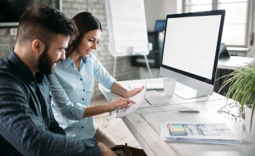 Beispielfoto: Zwei Personen sitzen gemeinsam am Schreibtisch bei der Arbeit am PC.