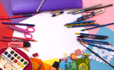 Stifte, Scheren und Farben sowie buntes Papier kreisförmig und farblich sortiert angeordnet.