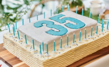 Foto: rechteckige, weiße Torte, belegt mit der türkisfarbenen Zahl 35, eingerahmt mit vielen kleinen türkisfarbenen Kerzen. 