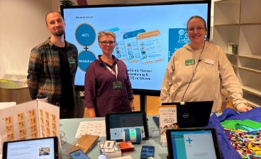 Foto: Drei IT Scouts der faw Lübeck bei der Veranstaltung BERUFSWELTEN. Auf dem Tisch vor ihnen: Infomaterialien, mehrere Tablets sowie ein Laptop.