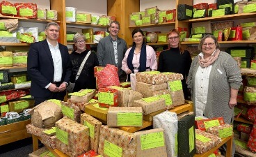 Foto: Sechs Personen stehen lächelnd inmitten vieler Weihnachtspakete anlässlich der Wunschbaumaktion im Sozialladen.