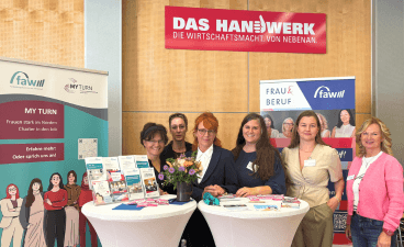 Foto: Beraterinnen von My Turn und FRAU & BERUF am Messestand. Vor Ihnen zwei Auslagetische, daneben Roll-ups.