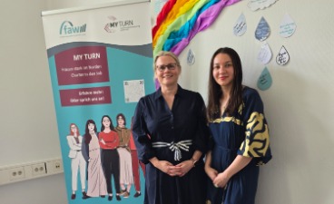Foto vom Diversitytag 2026 in der faw Lübeck: Zwei Personen nebeneinander vor einer bunt dekorierten Wand. 
