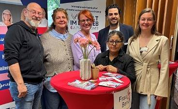 Gruppenfoto vom Messebesuch in Geesthacht: Sechs Personen stehen um einen rot eingedeckten Stehtisch.