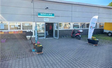 Foto: Gebäude „NOVI-LIFE“ mit zwei Pflanztöpfen sowie einem aufblasbaren Werbeaufsteller rechts und links vor der Eingangstür.  