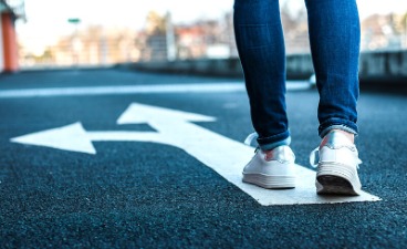 Foto: Straßenpfeil mit Abbiegung und einer Person, die sich auf den Weg macht.