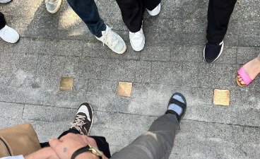 Foto von oben auf Beine, Füße und Stolpersteine auf dem Boden.