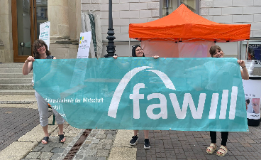 Drei Frauen halten ein FAW Banner nach oben.