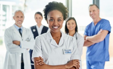 Beispielfoto: Fünf Personen in medizinischer Arbeitskleidung stehen im Halbkreis u. blicken lächelnd in die Kamera. 