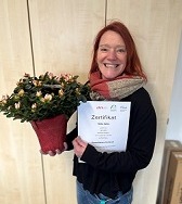 Herzlichen Glückwunsch, Heike Seiler! Foto von Heike Seiler mit Blumen und Prüfungszertifikat.