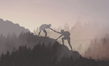 Beispielbild: Zwei Menschen beim Klettern, einer zieht den anderen hoch; neblige Berglandschaft im Hintergrund.