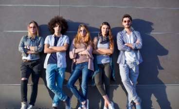 Beispielfoto: Fünf Jugendliche lehnen Seite an Seite mit verschränkten Armen an einer grauen Wand. 