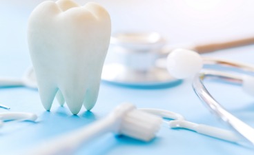 Foto: Modell eines Zahns mit Zahnbürste, Zahnpasta und Stethoskop auf blauem Hintergrund, Symbol für Zahn- und Mundgesundheit.