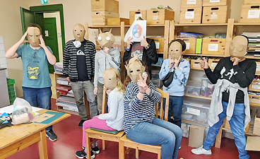 Gruppe von Kindern hält sich Papiermasken vors Gesicht